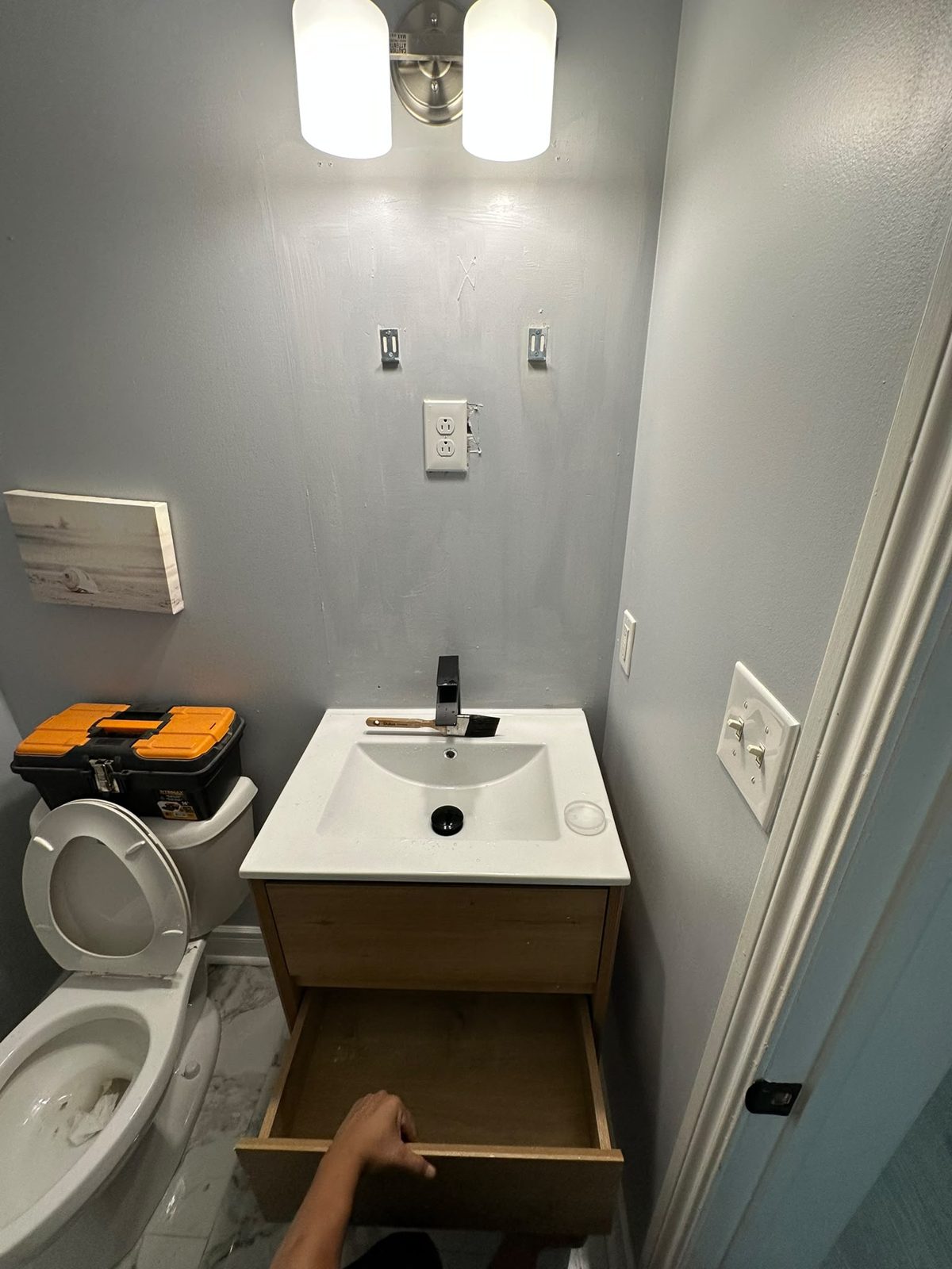 Two-drawer wood vanity with white sink being installed in a compact Toronto-area bathroom