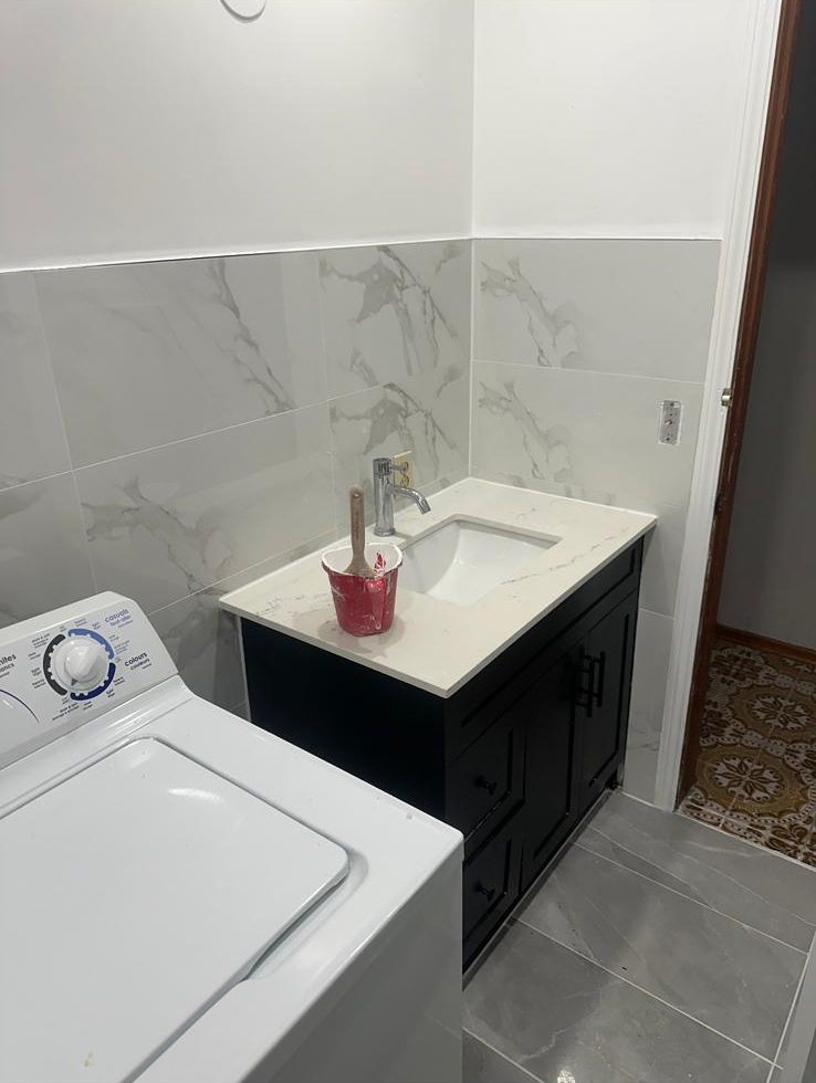 Black bathroom vanity with white top and marble-look porcelain wall tile wainscot next to the washer, GTA bathroom update