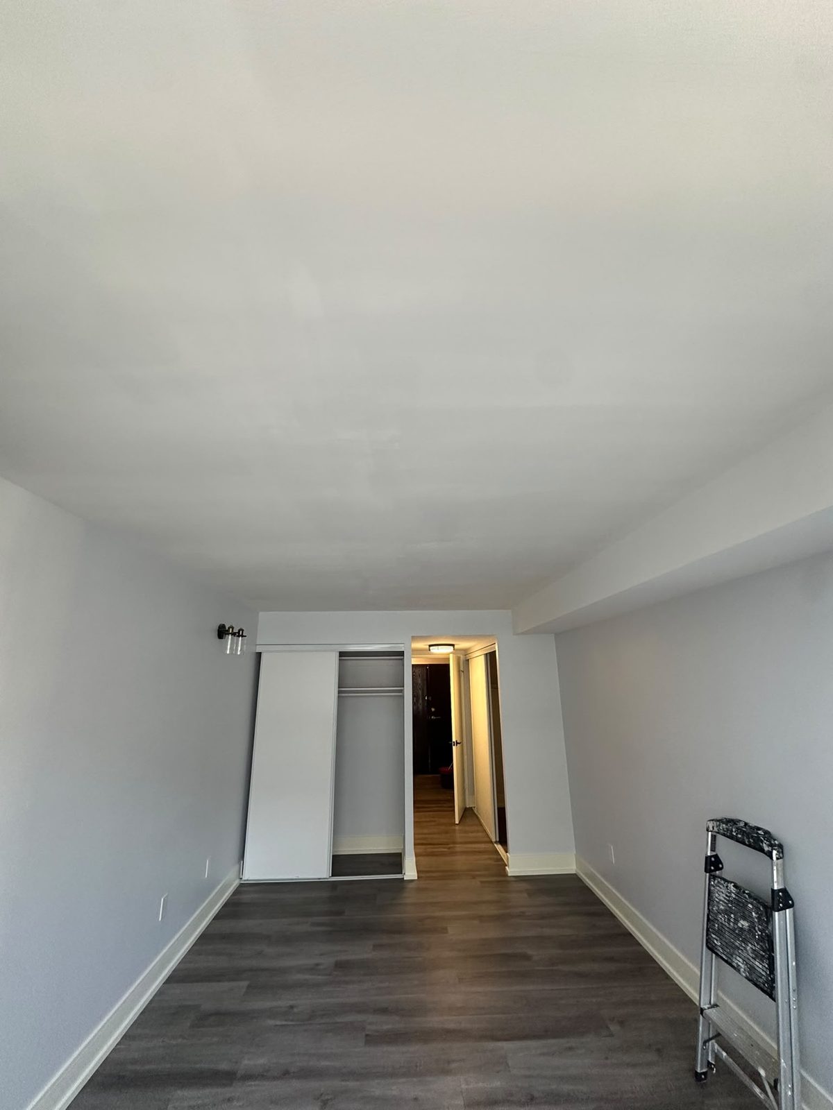 Dark grey vinyl plank flooring in a freshly painted condo bedroom looking toward the hallway, Toronto