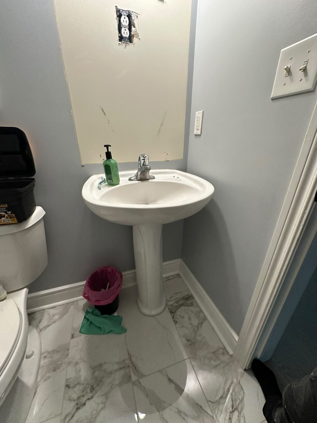 Powder room with a white pedestal sink and polished marble-look porcelain floor tile, Toronto-area home renovation