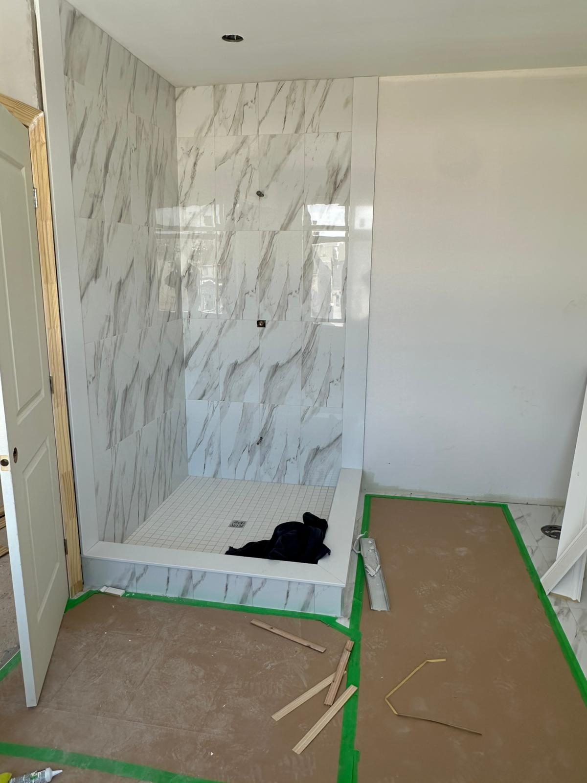 Marble-look porcelain tile walk-in shower during installation with floor protection in place, GTA bathroom renovation in progress